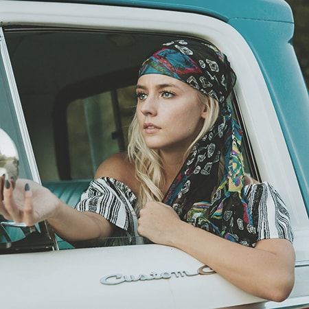 Woman inside a blue colored car, is wearing a cap, covering her blond hair.