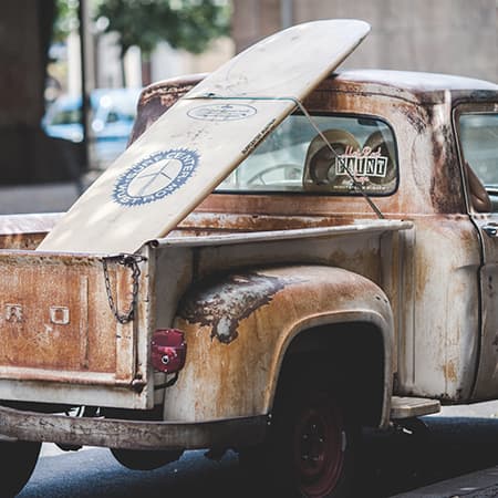 Photo of an old pickup truck, with a surfboard in the back.